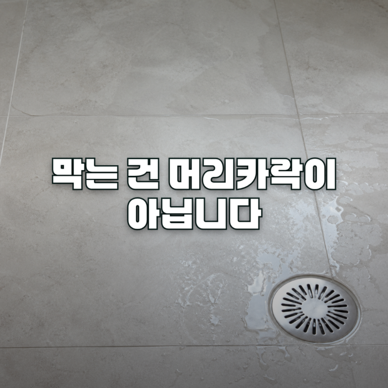A close-up overhead view of a clean tiled bathroom floor with a round stainless steel floor drain cover slightly off to